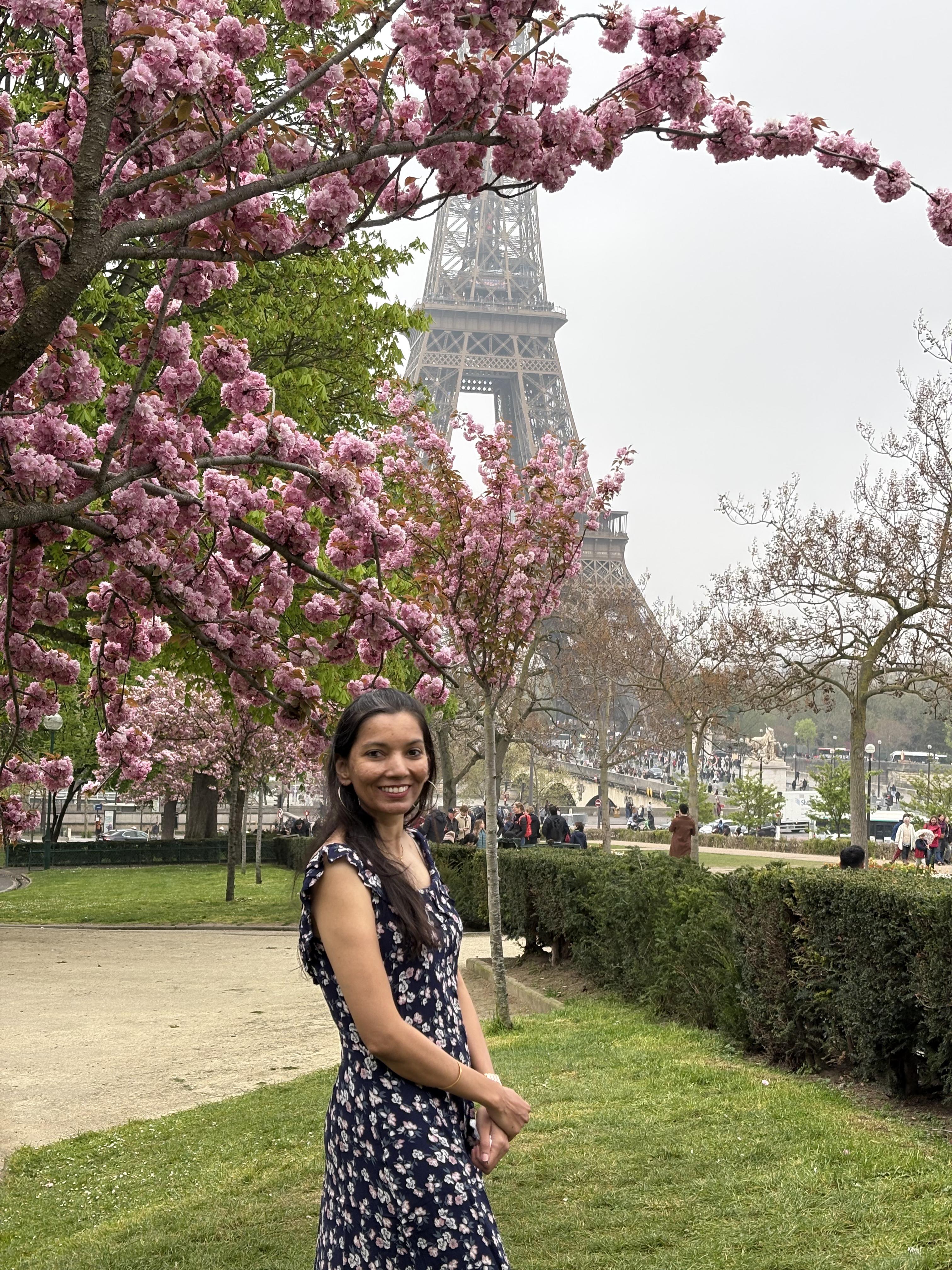 Picture of a beautiful woman standing under cherry blossoms in Paris, with the Eiffel tower in the background